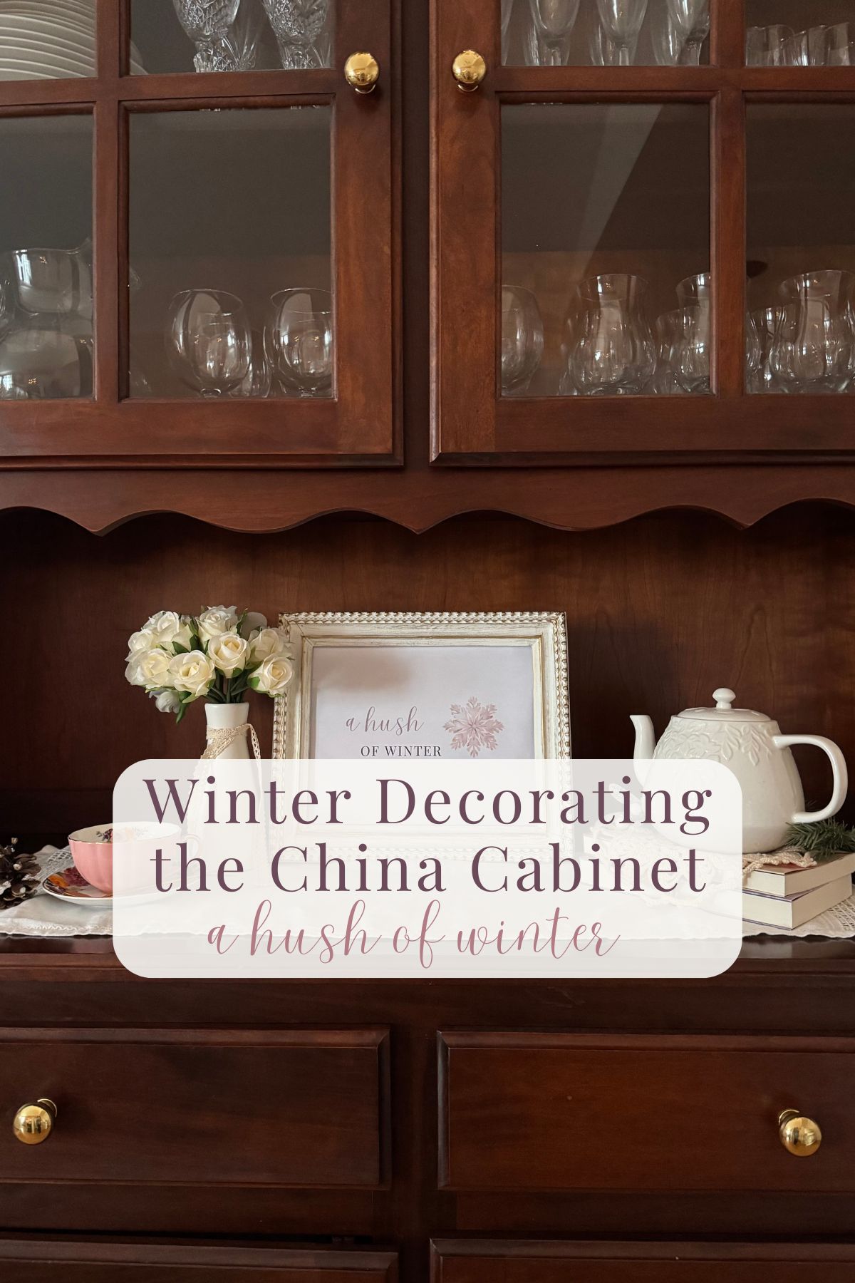 Winter Decorating the China Cabinet -a hush of winter. A framed sign, teapot on a stack of books, flower vase in a cherry wood china cabinet.