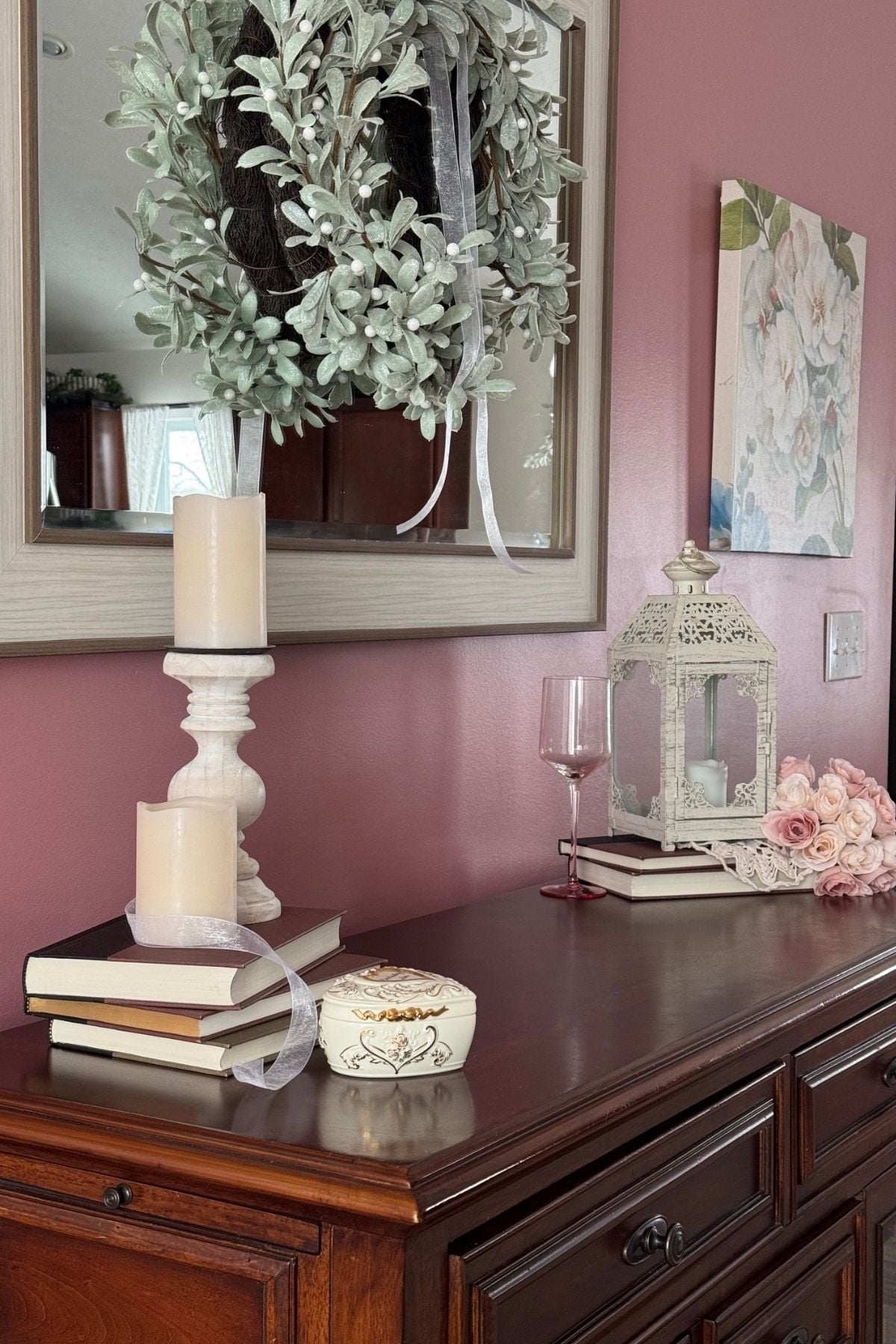 Romantic blush and ivory sideboard decor for winter: lantern, wooden candle holder, stacks of books, heart-shaped musicbox
