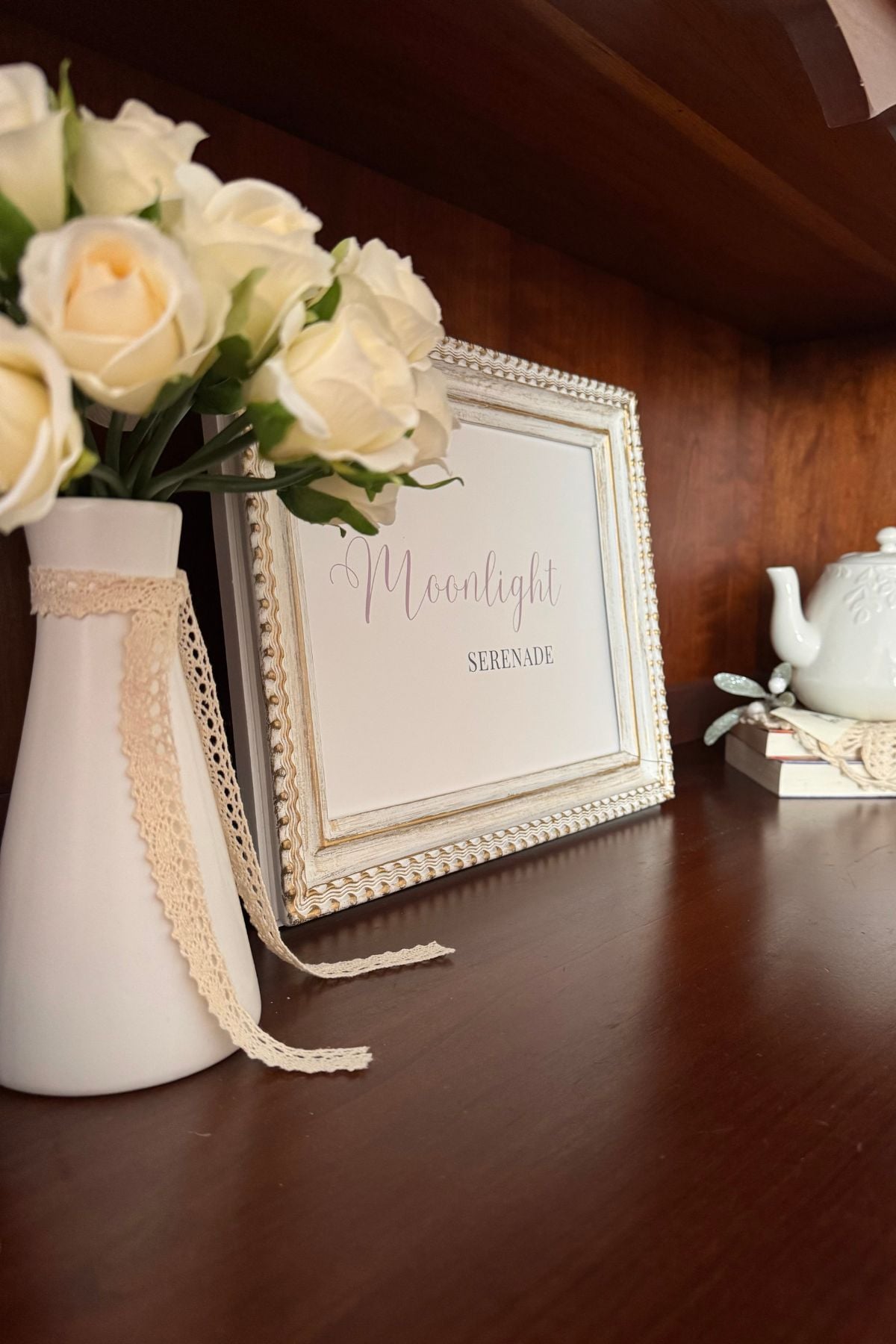 Moonlight Serenade framed sign in china cabinet next to ivory roses in a white vase