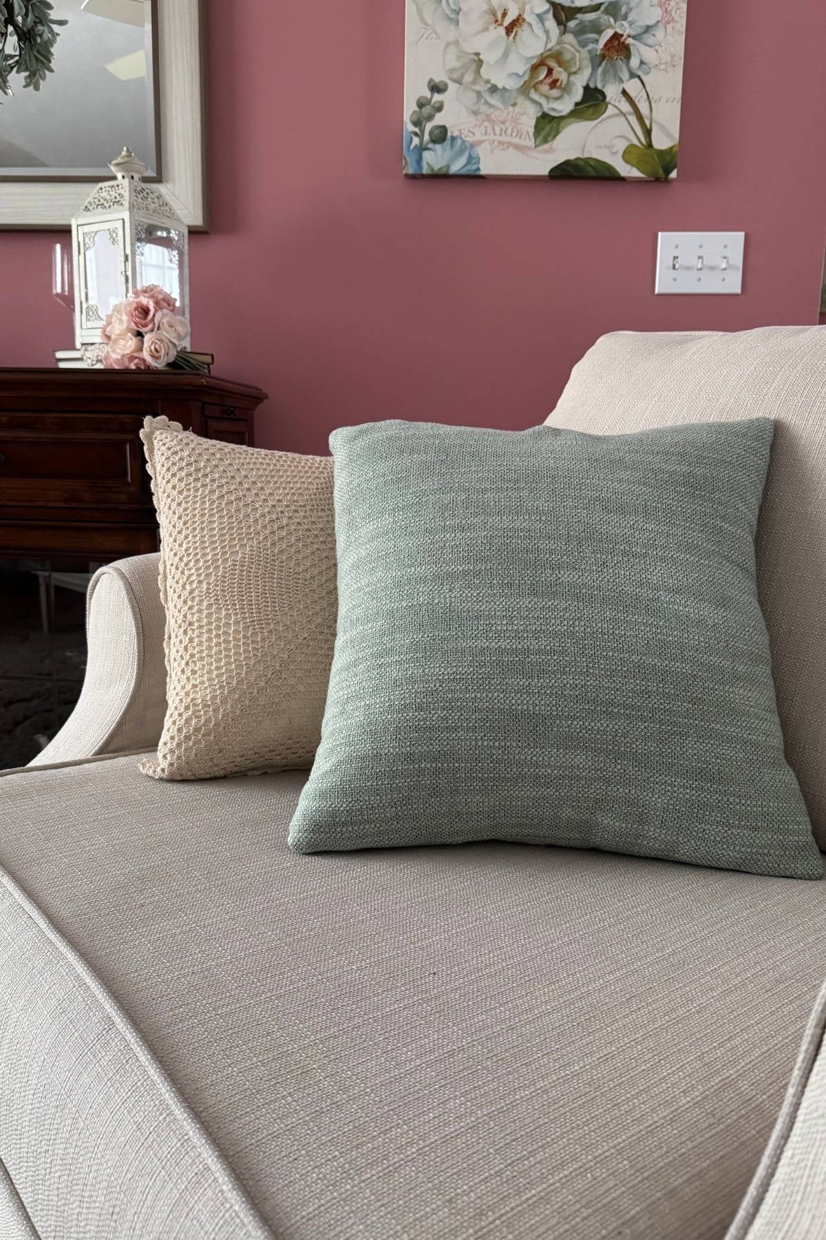 soft sage and a crocheted throw pillows on an arm chair in a living room with rose colored wal;
