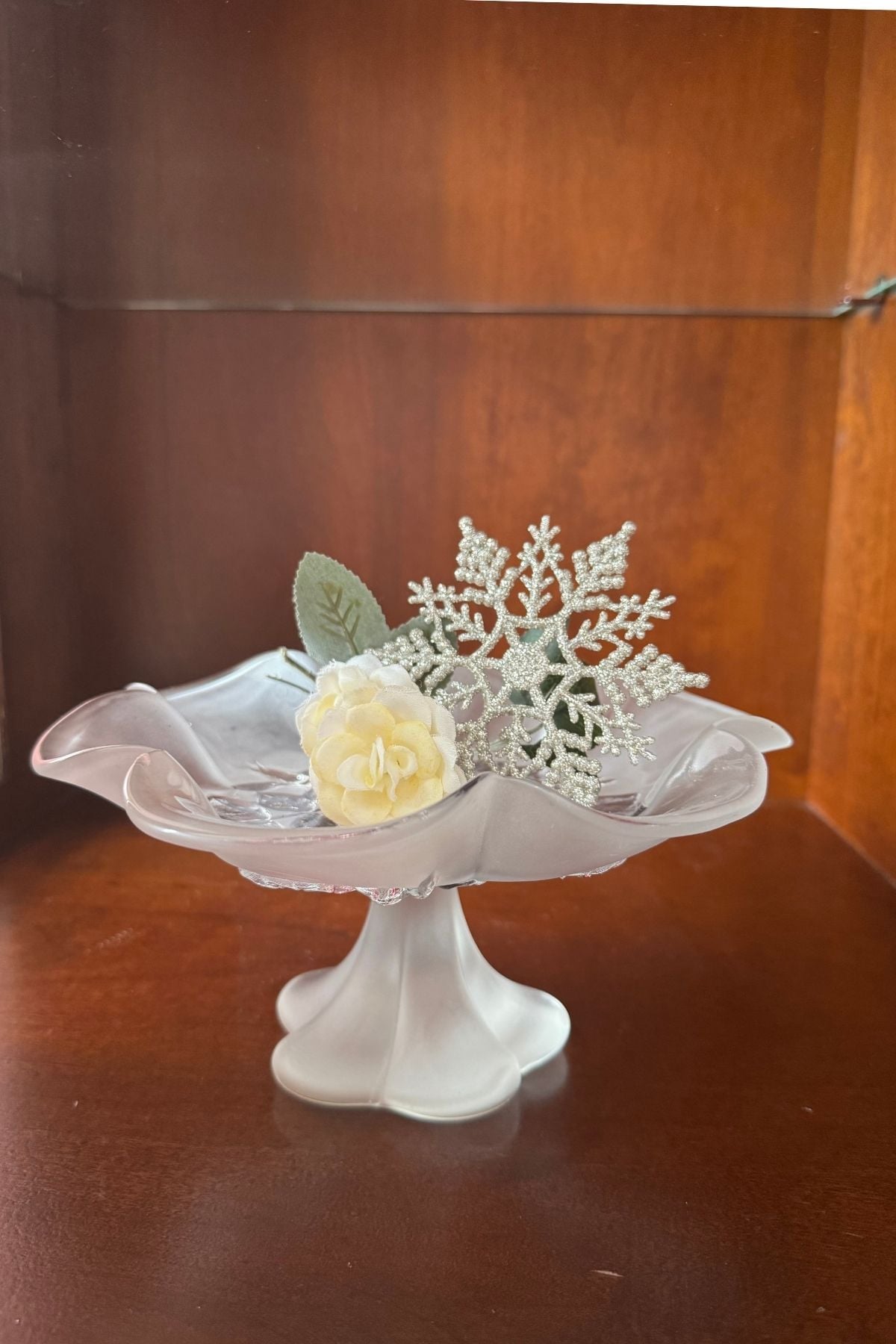 A soft white rose on a scalloped, frosted glass pedestal