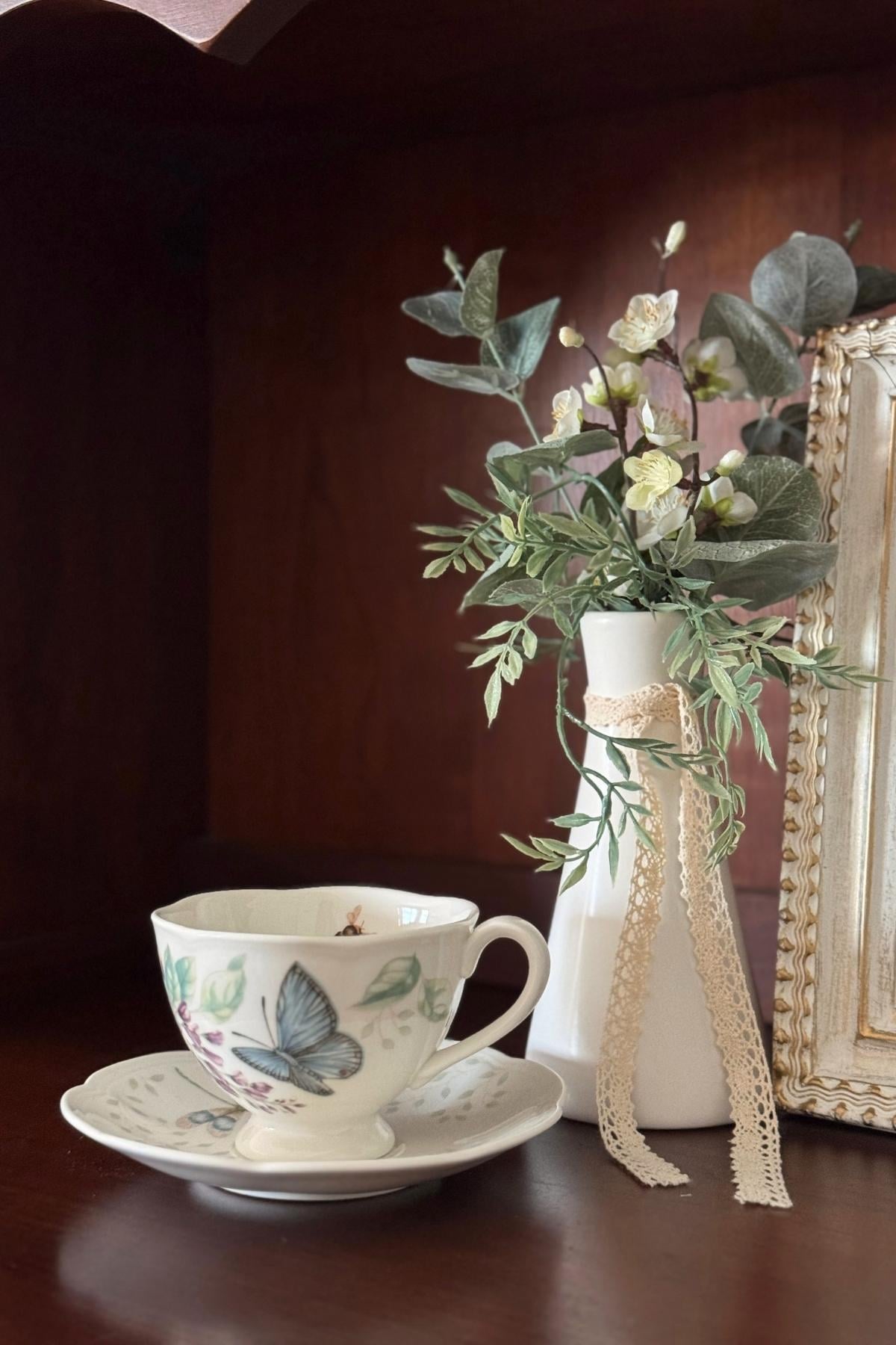 Greenery and white flowers in a white ceramic vase.