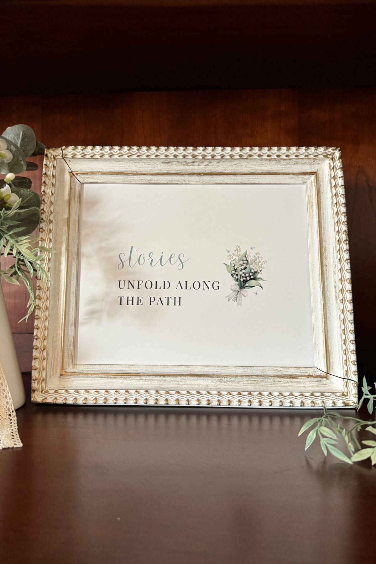 Framed storybook sign: Stories Unfold Along the Path. A lily of the valley design.