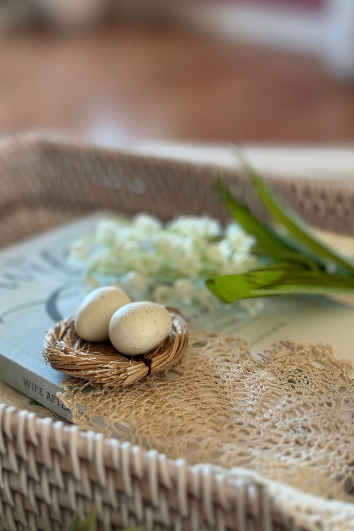 A tiny decorative nest with two speckled eggs on a beige doily.