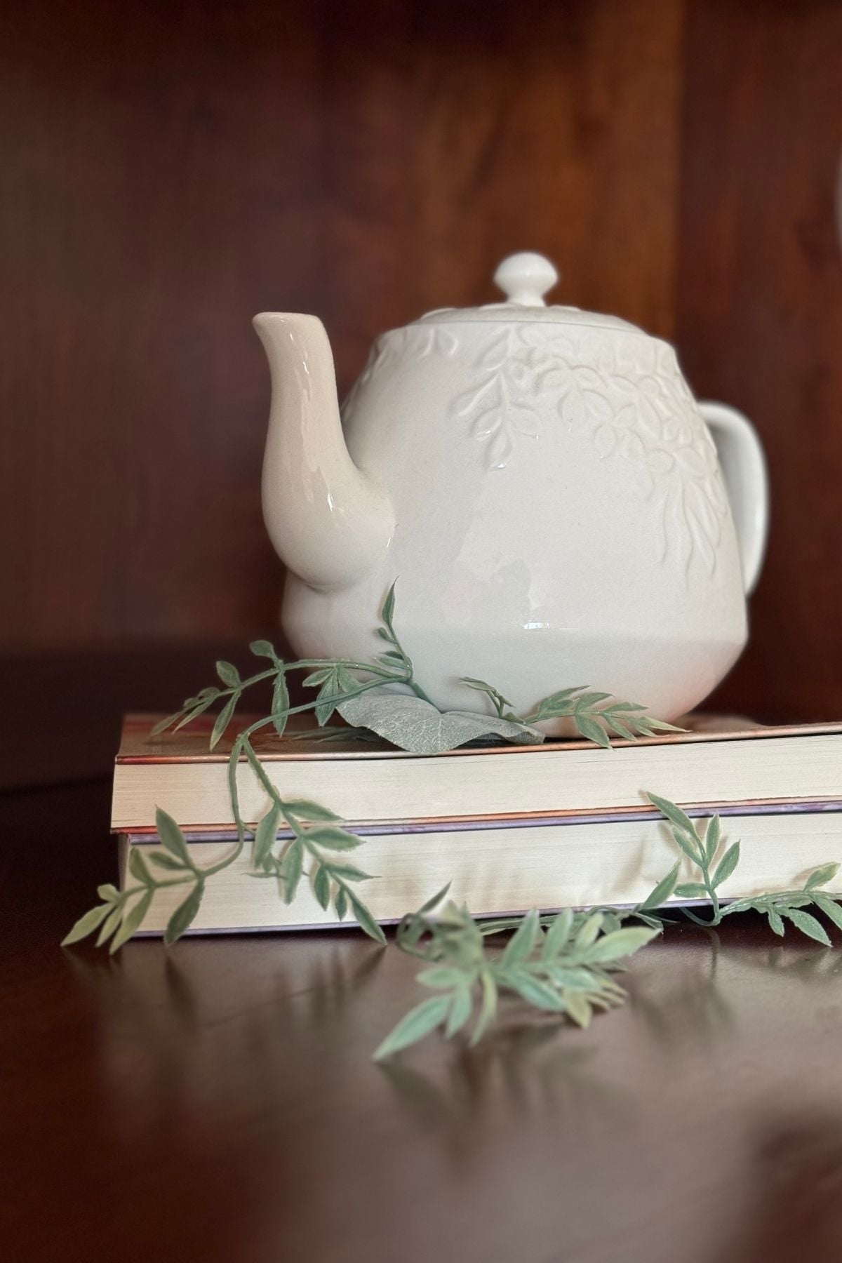 White ceramic teapot and spring greenery on books