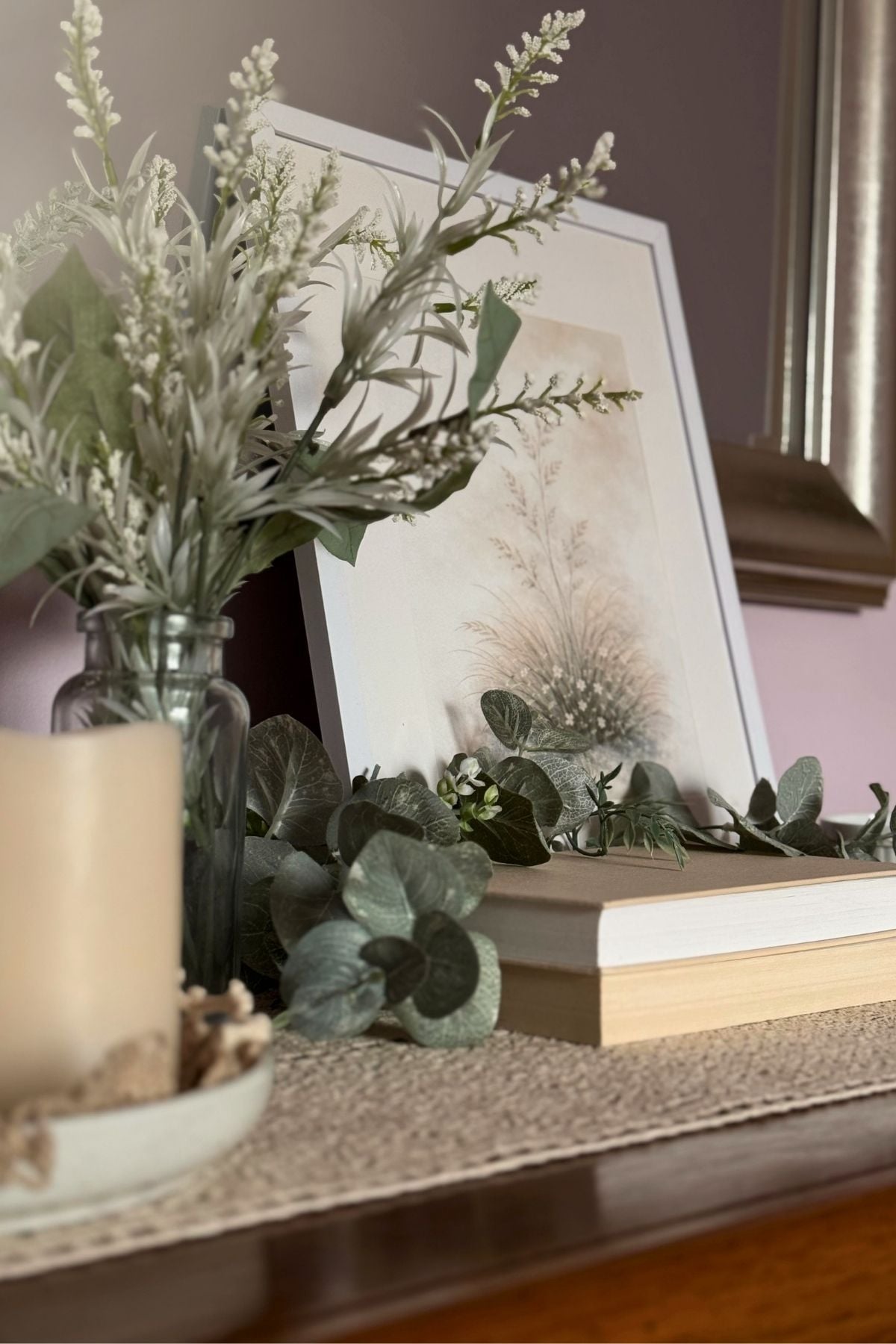 Layered spring bedroom vignette with soft greenery, stacked books, and botanical artwork