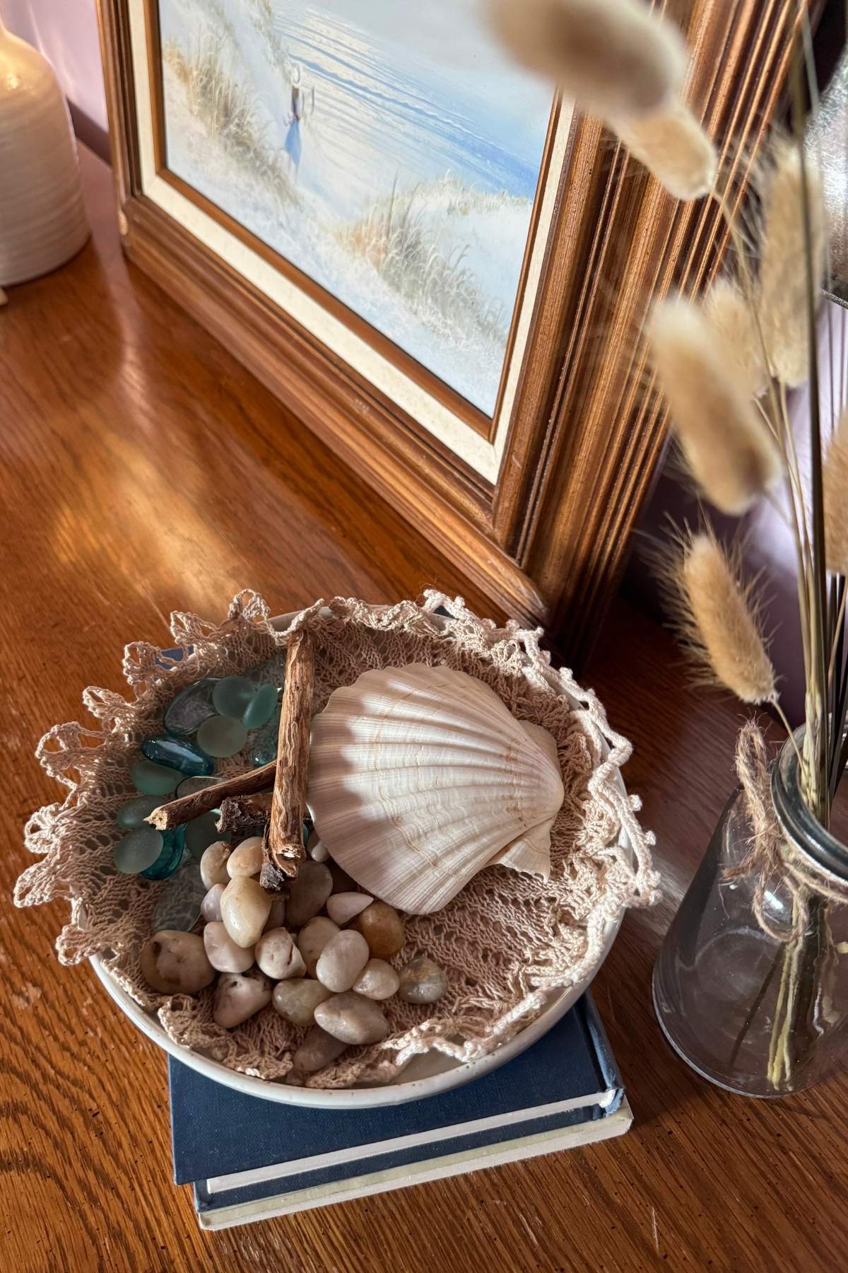 Simple coastal decor on a dresser: stacked books, ceramic plate layered with a doily holding collected treasures