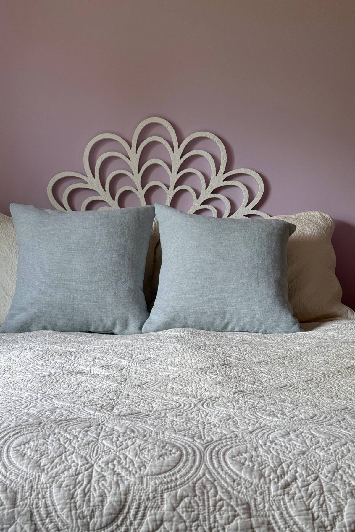 Cream embossed quilt and misty light blue throw pillows in a small master bedroom