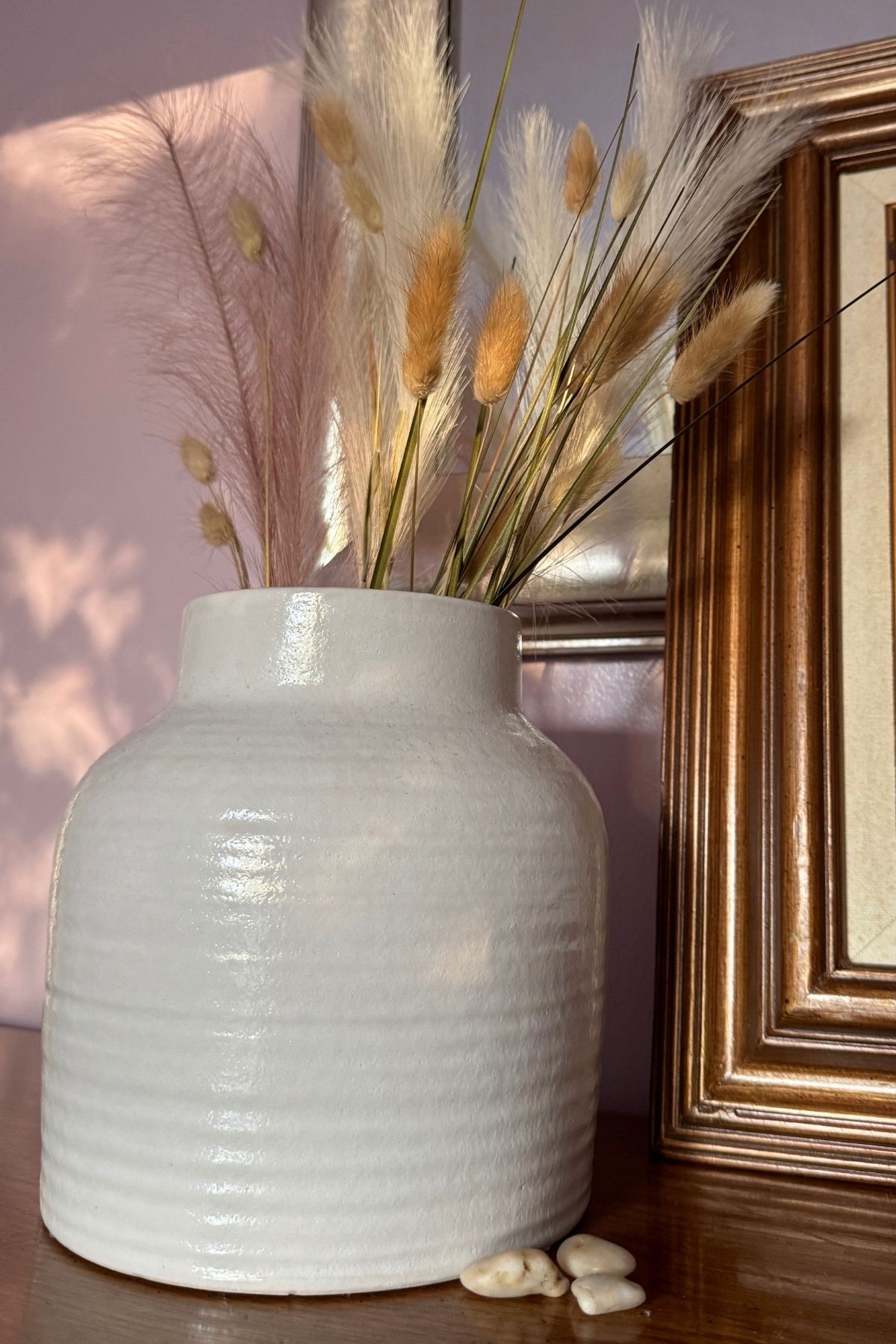 Pampas grass and weathered grass in a cream crock. A couple of smooth pebbles nestled next to it.