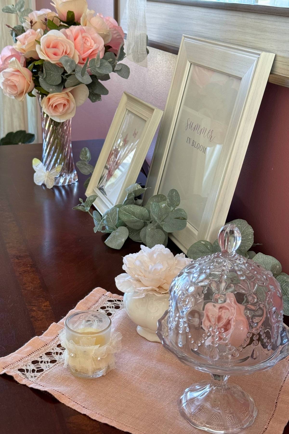 summer cottage decor on dark wood credenza Summer cottage decor on dark wood sideboard: pink roses, white frames for art, glass cloche, candle, sugar bowl.
