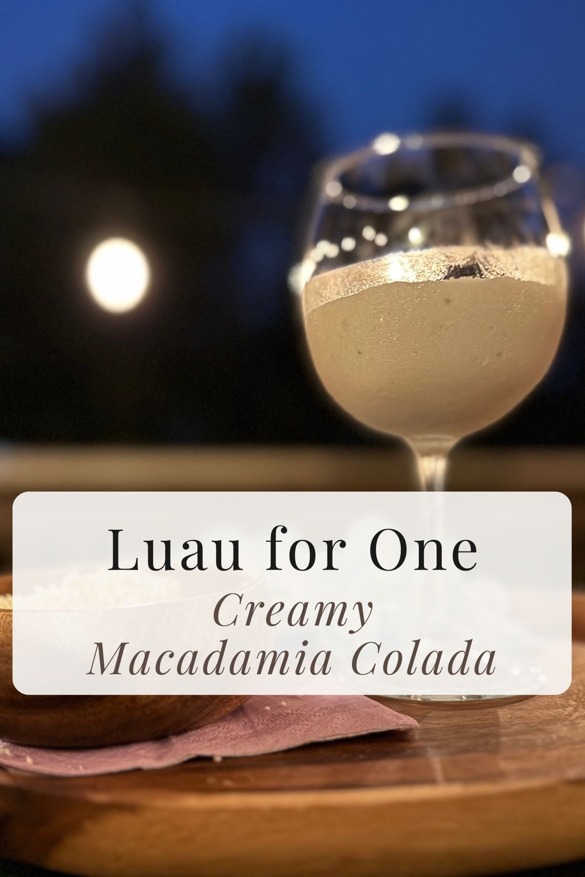 Creamy Macadamia Colada smoothie with tropical luau decorations on an outdoor table at sunset.