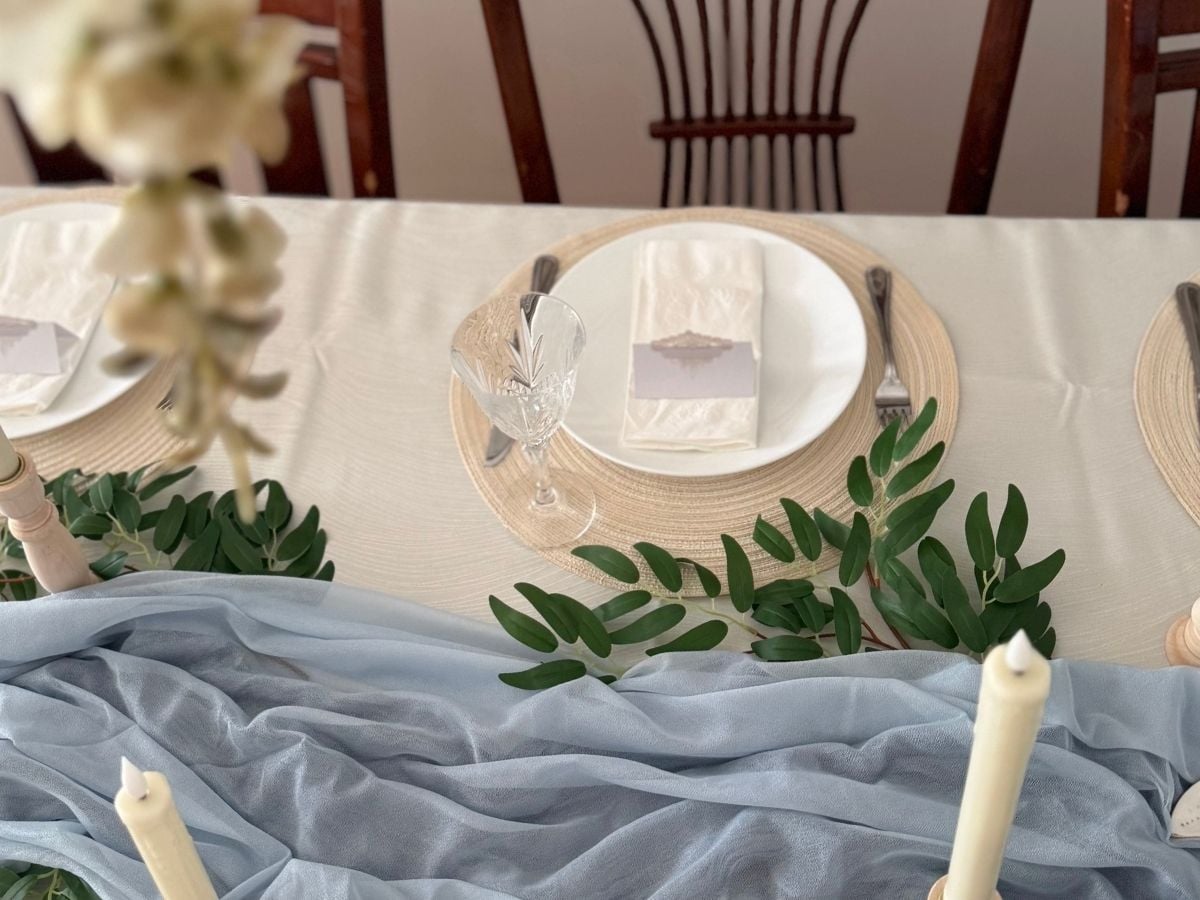 Rivendell-inspired-table-setting A chiffon table runner, greenery tucked in, white plate, and a crystal wine glass on an ivory placemat