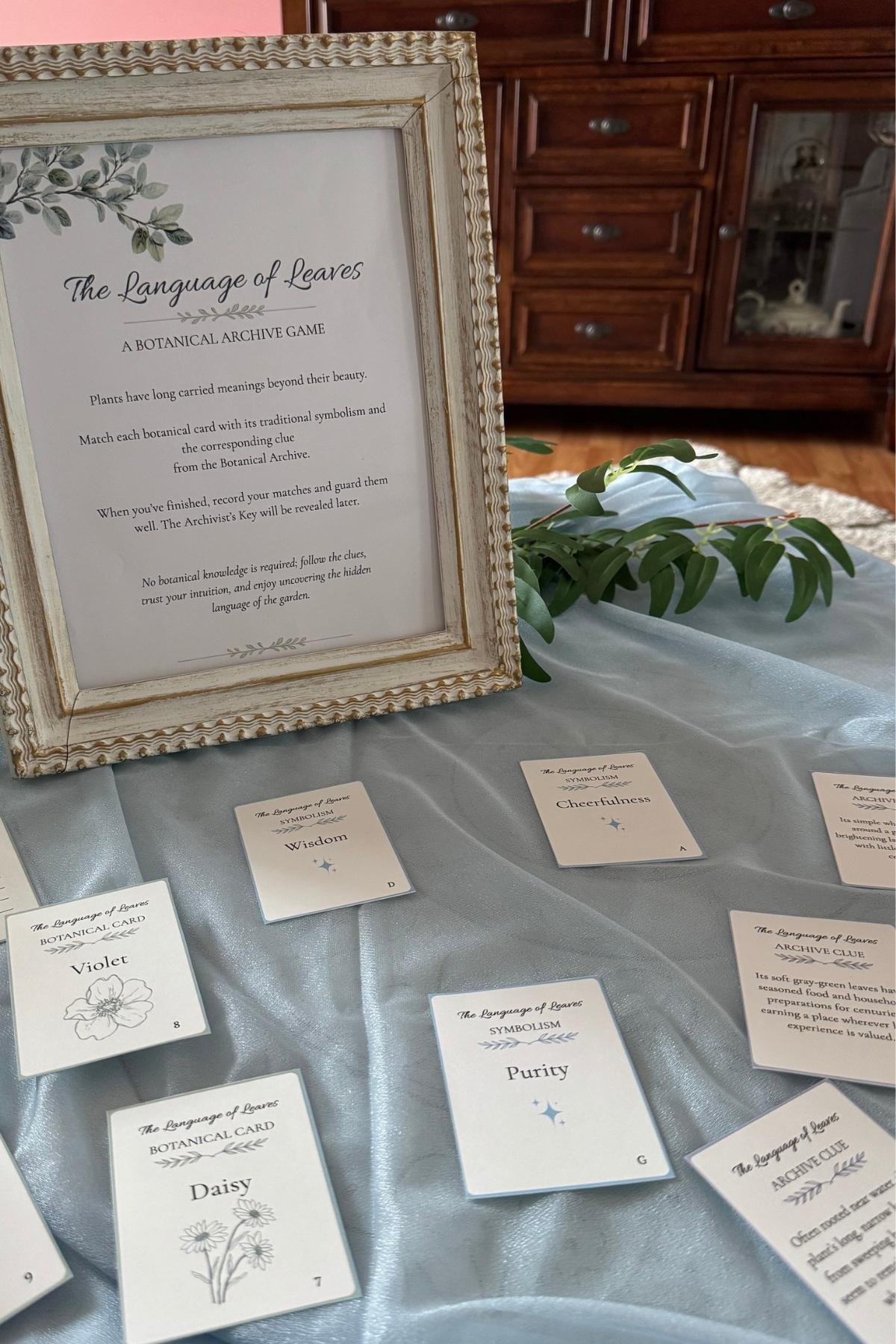 language of leaves game cards Language of the Leaves game sign and botanical cards spread across pale blue chiffon with greenery at the edge.
