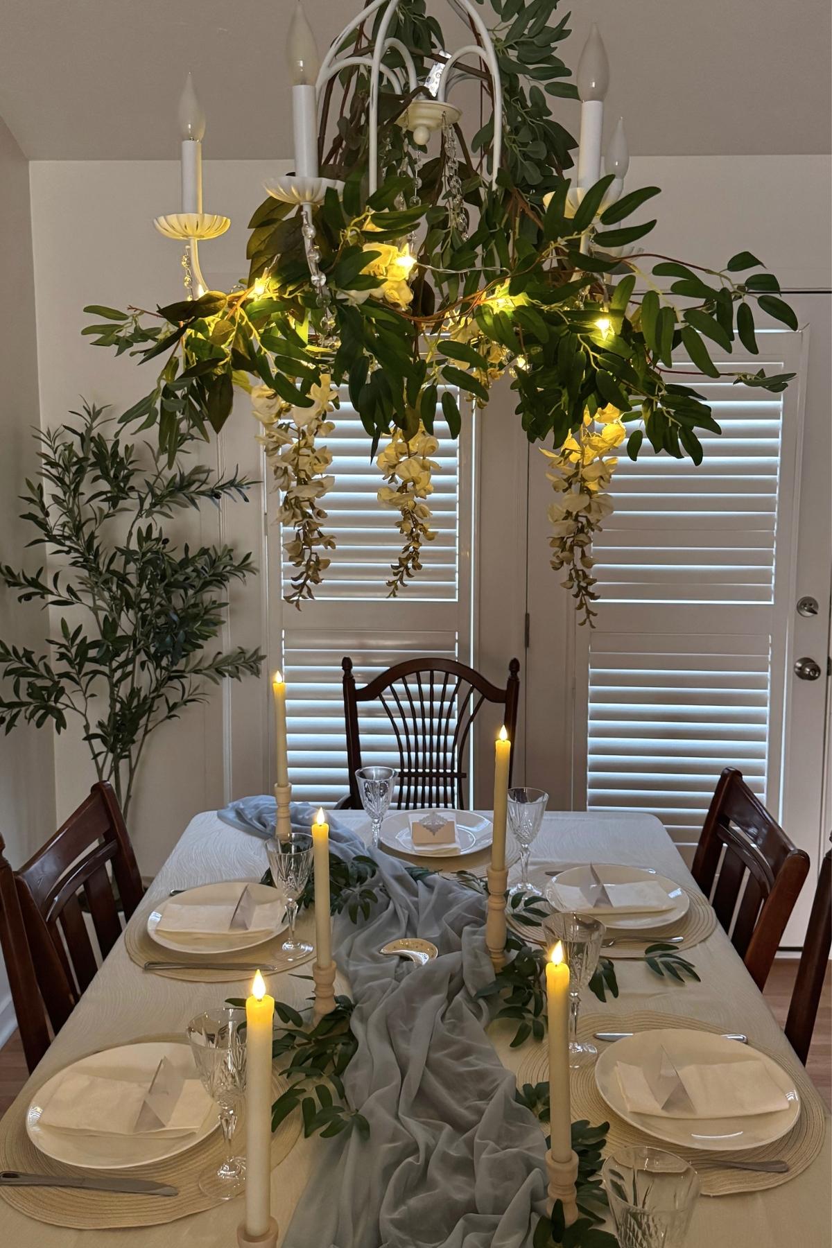rivendell-table-chandelier-daylight Daytime view of a Rivendell-inspired table beneath a chandelier draped with greenery and white wisteria.