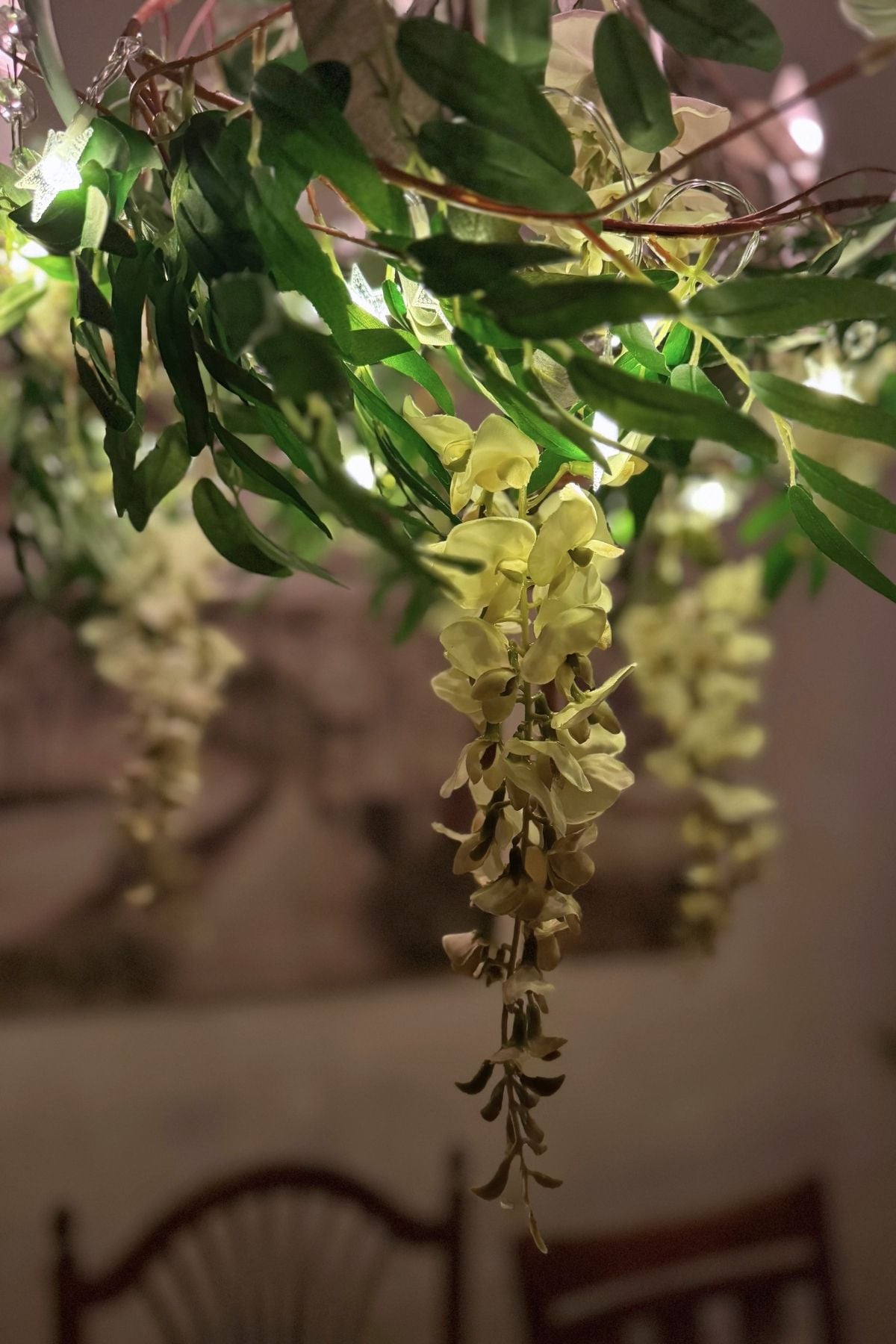 white-wisteria-chandelier-closeup Close-up of white wisteria, greenery, and tiny star lights hanging from the decorated chandelier.