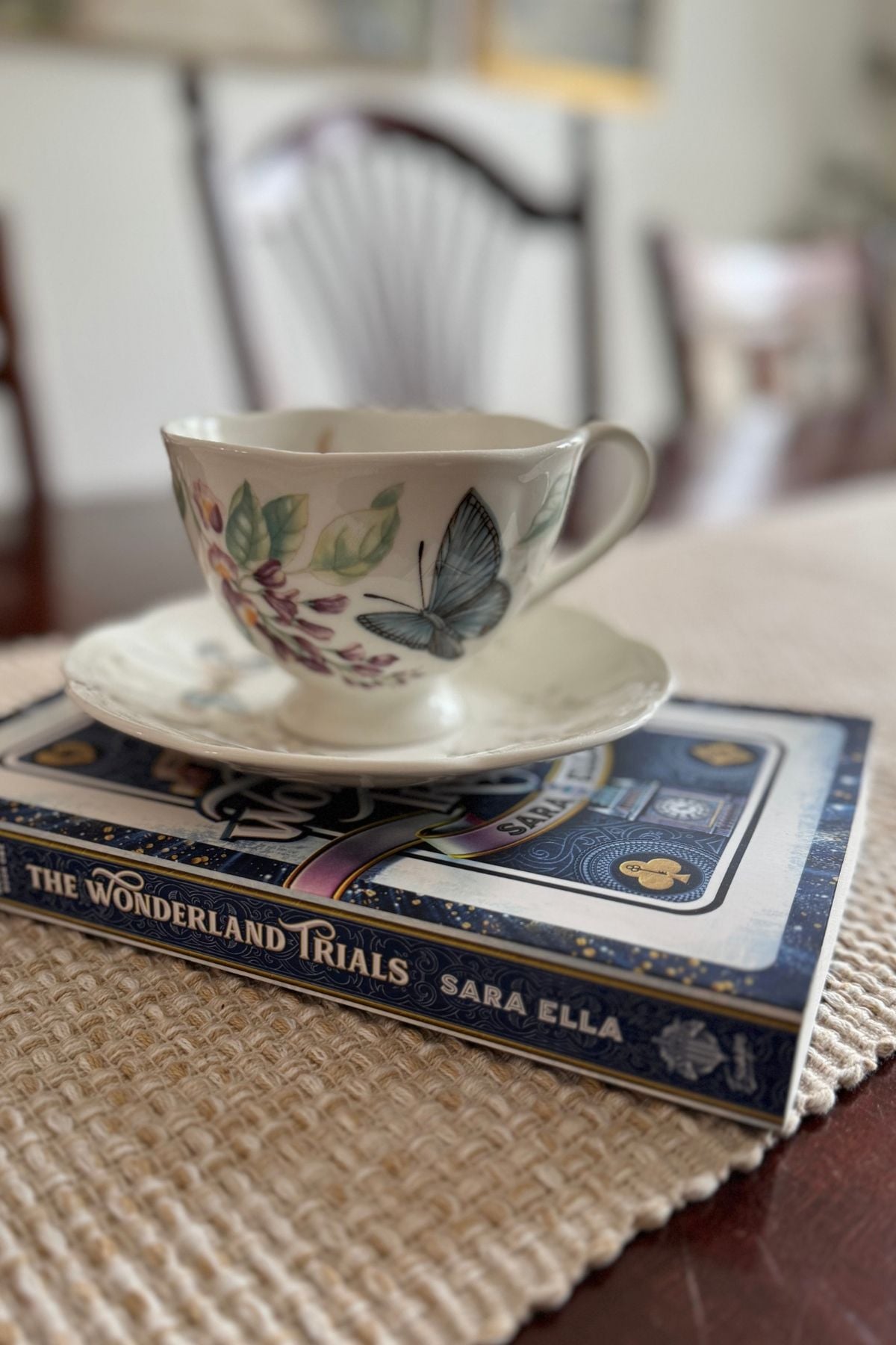 A teacup on the book, The Wonderland Trials by Sara Ella