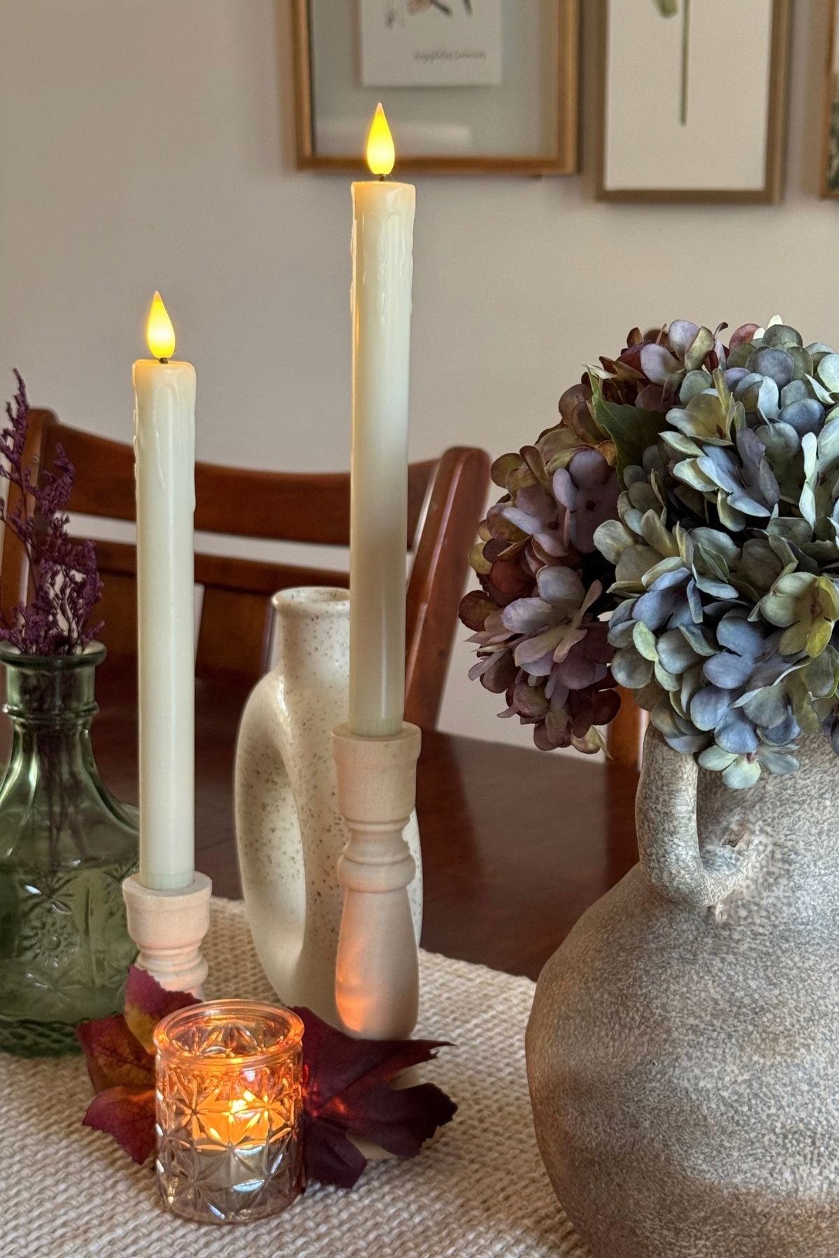 Amber gold votive candle holder tucked beneath wooden candle holders with cream taper candles.