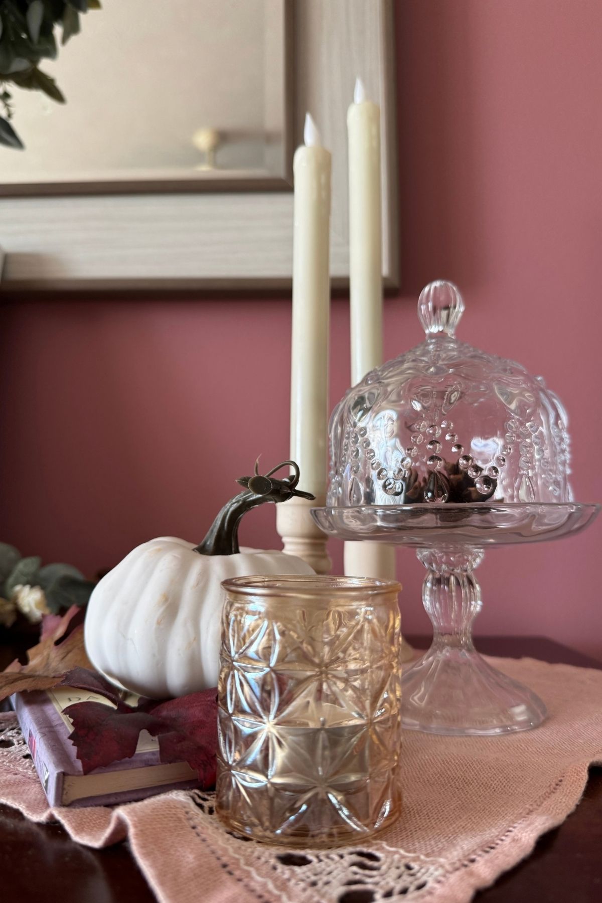 autumn decor on a sideboard Autumn decor, such as a cream pumpkin, amber-gold votive candle holder, cream tapered candles, and a glass cloche holding a pinecone,