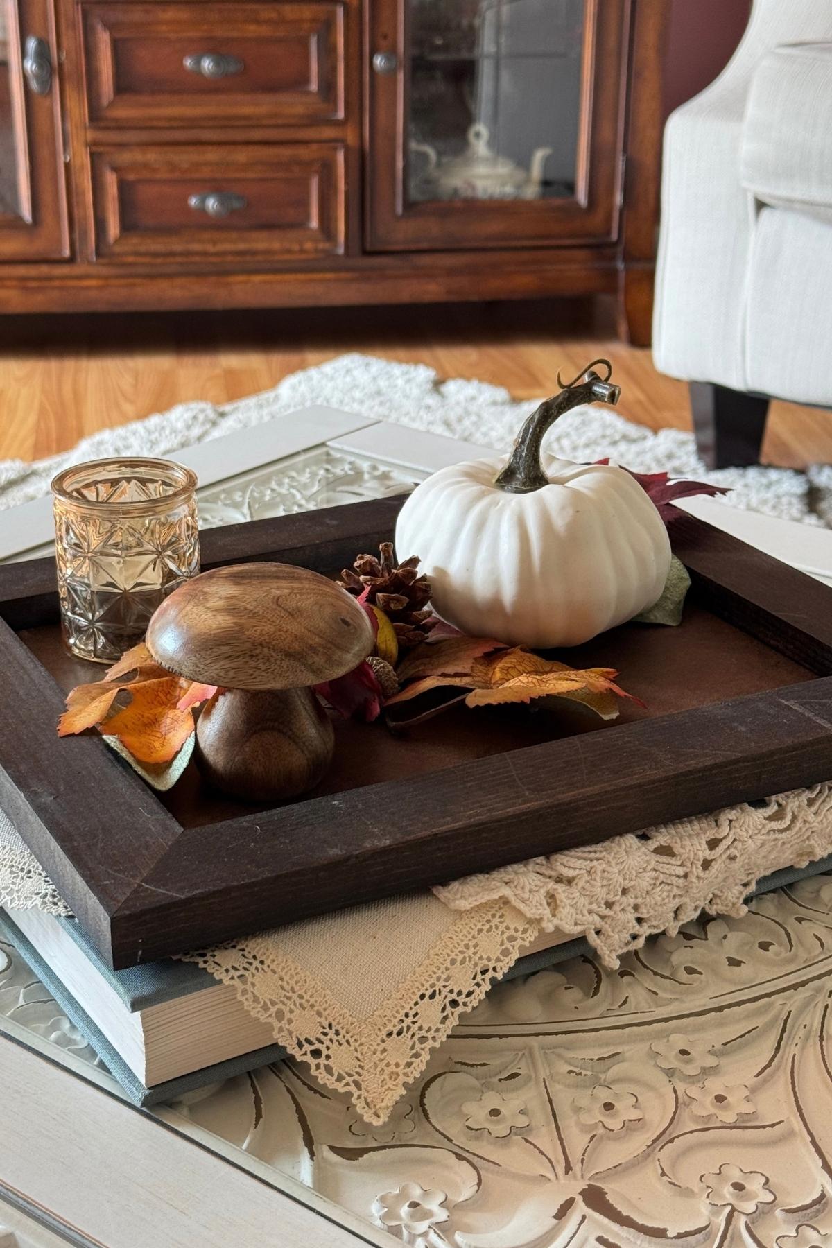 fall coffee table decor tray (2) A fall decor tray on the coffee table with a cream pumpkin, amber gold candle holder, wooden mushroom, and autumn leaves