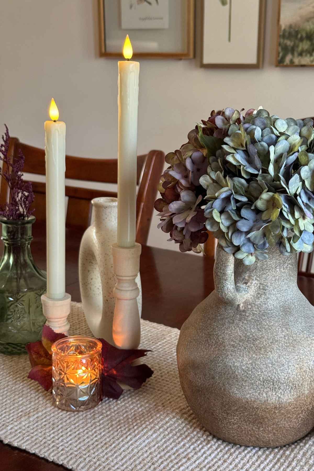 Romantic fall dining table centerpiece with faded hydrangeas, textured vases, and ivory taper candles.