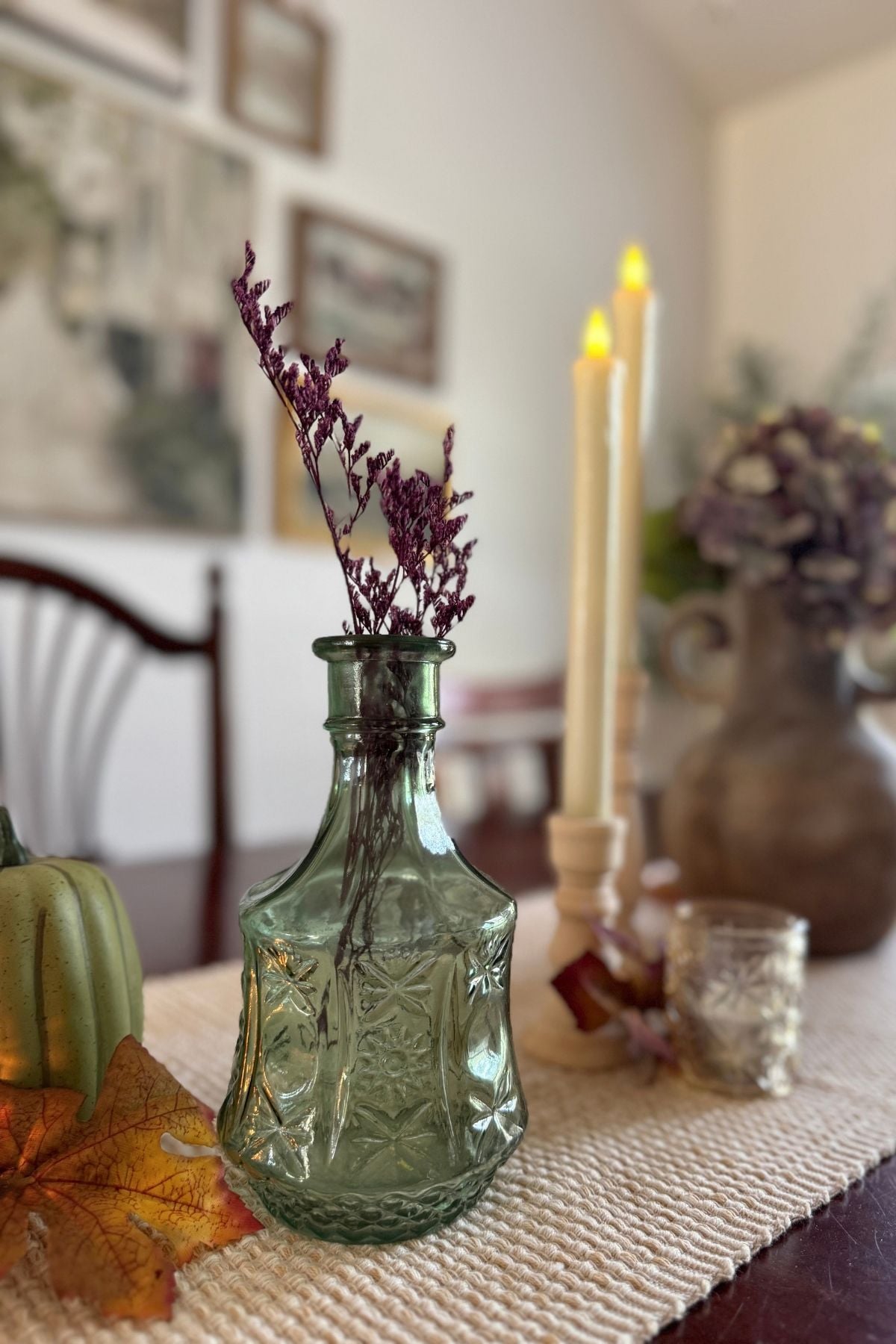 Green glass bottle and tapered candles on a woven table runner in the dining room.