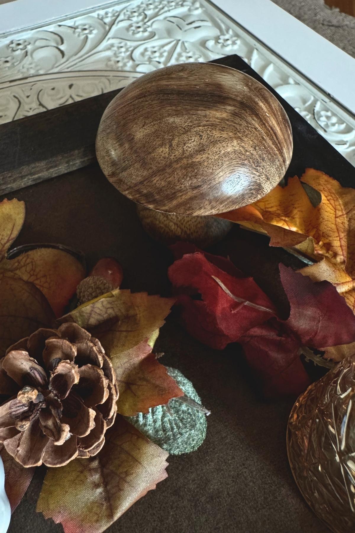 wooden mushroom on an autumn tray Storybook autumn decor on a dark tray, featuring a wooden mushroom, pinecone, autumn leaves